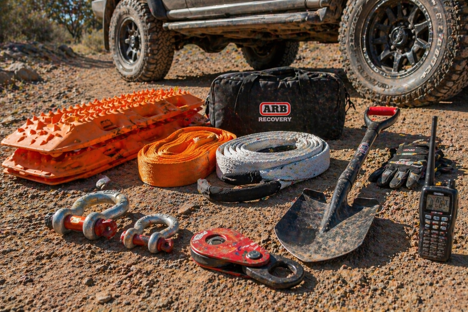 Ground-view spread of recovery gear (tracks, snatch strap, shackles, shovel, UHF).
