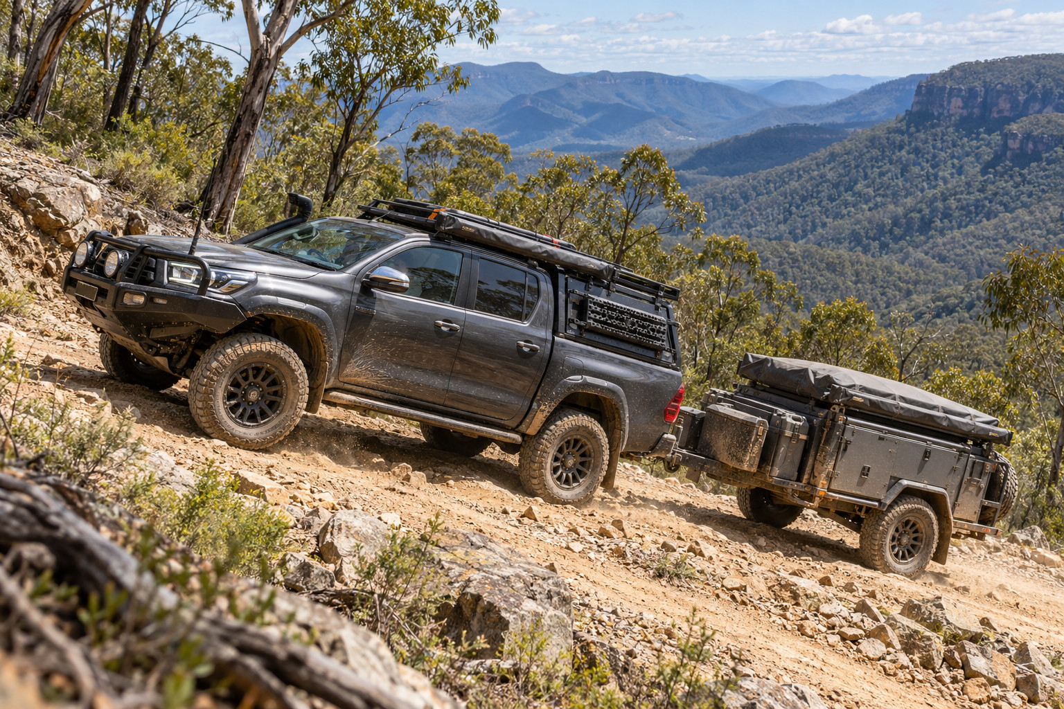 Modified 4WD towing a compact off-road camper up a steep mountain track.